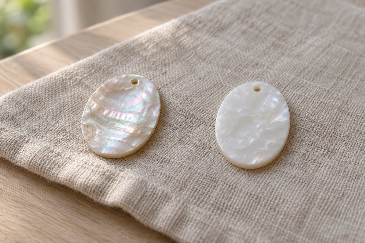 Pastille de vraie nacre irisée à côté d'une pastille de résine nacrée sur lin